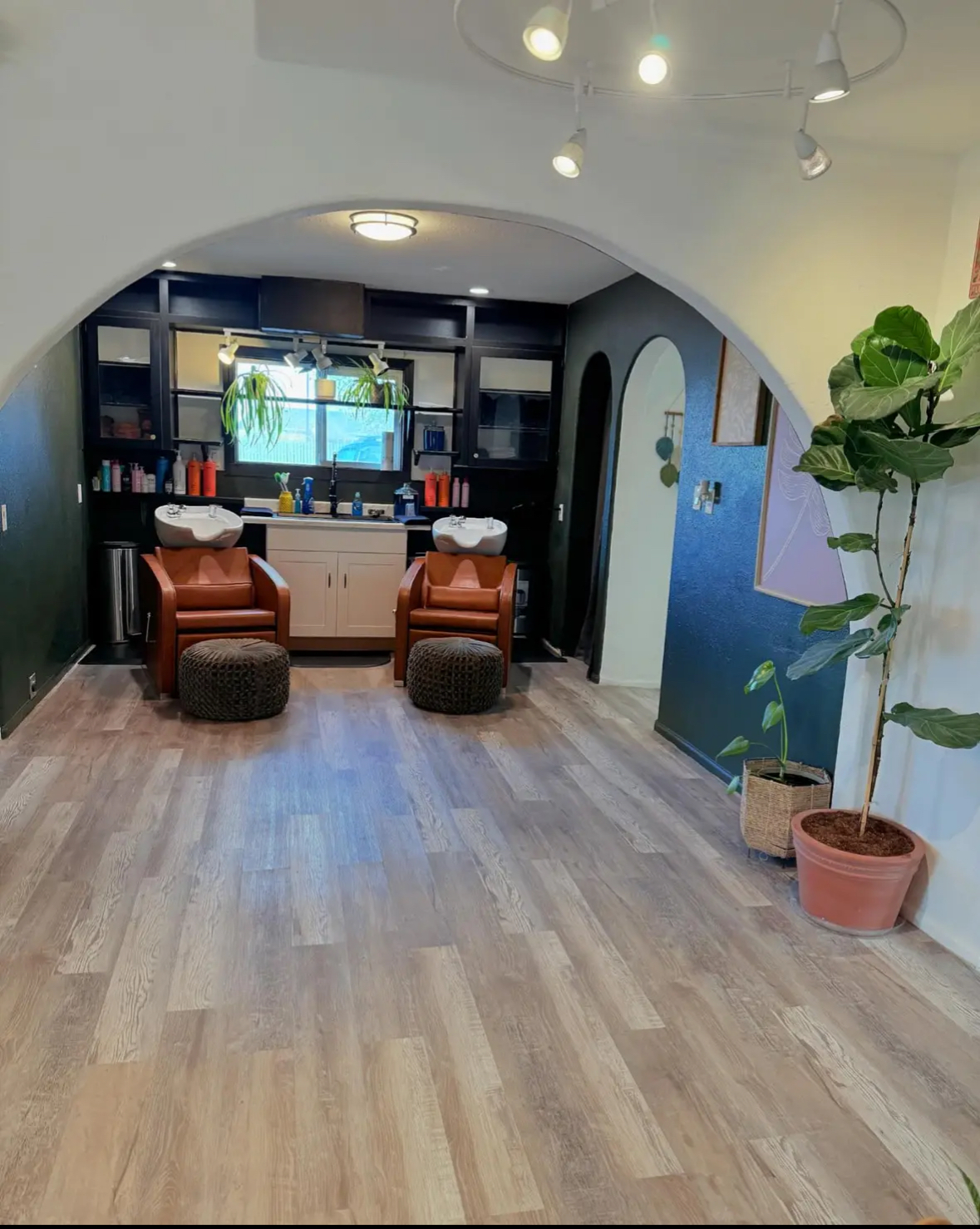 The wash station at Wildflower with cognac chairs, a deep teal wall, and a tall fiddle-leaf fig